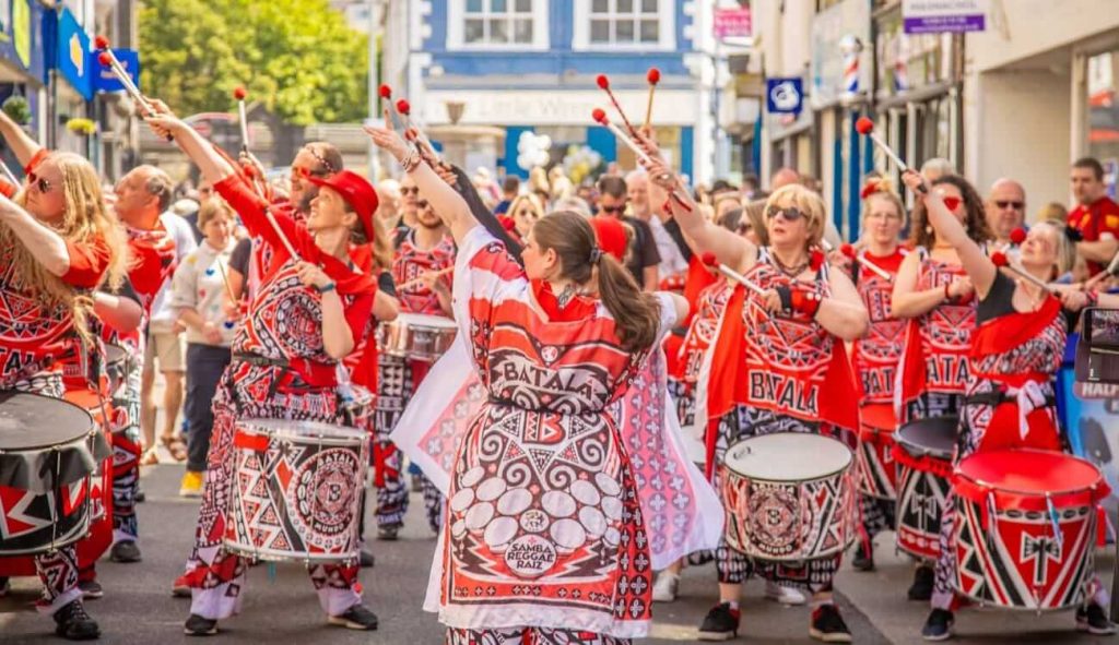 Batala Bangor performing in Caernarfon. The band all point their beaters up in the air.